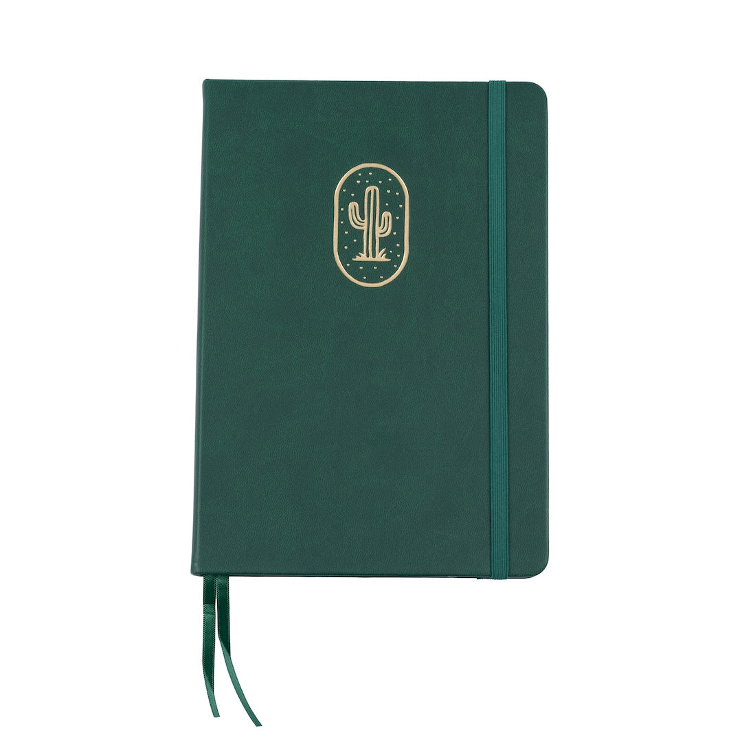 The A5 bobo Black Dot Grid Journal in "Cactus" with a dark green smooth vegan leather cover. A gold foil saguaro cactus illustration is stamped onto the front cover. A matching green ribbon bookmark and elastic closure can be seen.