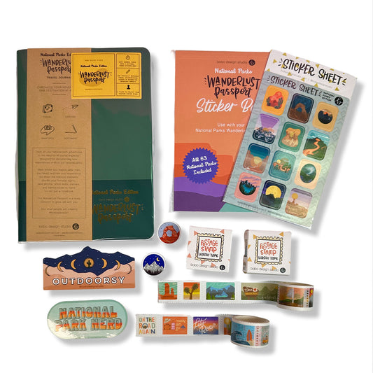 a dark green national parks wanderlust passport with a sticker that says outdoorsy and another sticker that says national park nerd below it. next to the passport is a national parks sticker book and a national parks sticker sheet on top of that. below the sticker sheets are two postage stamp washi tapes. underneath the washi tape boxes the two washi tapes are rolled out