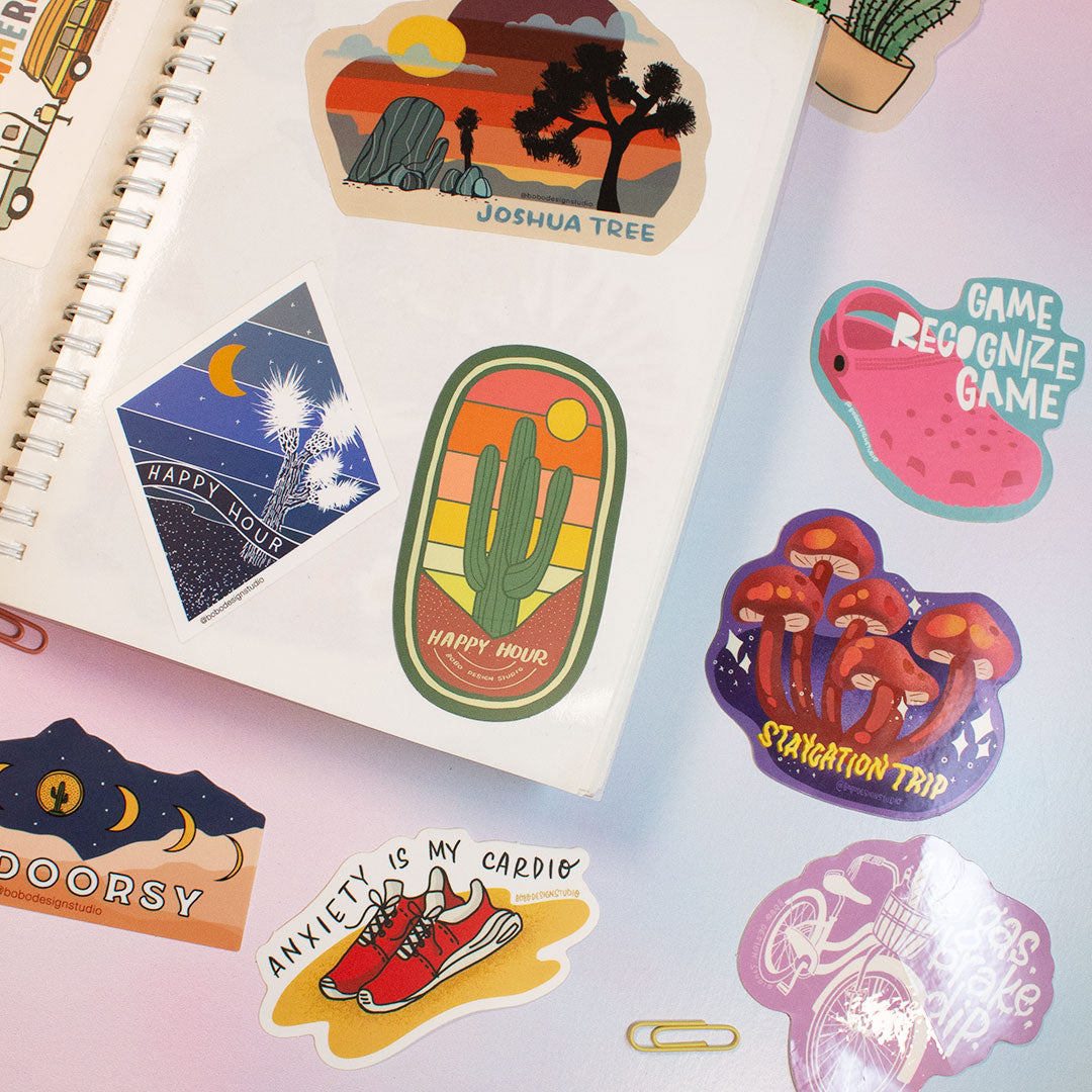 zoomed in image of open page of reusable sticker book with three stickers on the right page and one showing slightly on the left two stickers under the book and three to the right and one showing slightly on top right corner of book