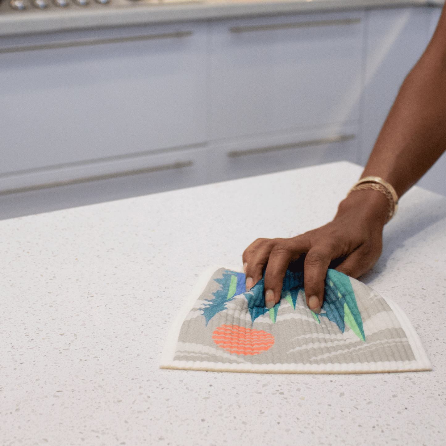 Hand using Pacific Northwest Sponge Cloth to wipe a kitchen counter. Sponge cloth is flexible and is softly crumpled in the hand's grasp.