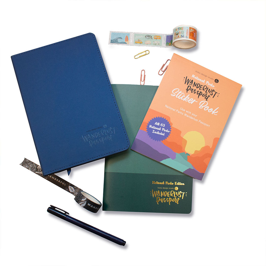 a blue wanderlust passport and a national parks sticker book on top of a national parks wanderlust passport with a rolled out washi tape and three paper clips above and a rolled out washi tape and pen below