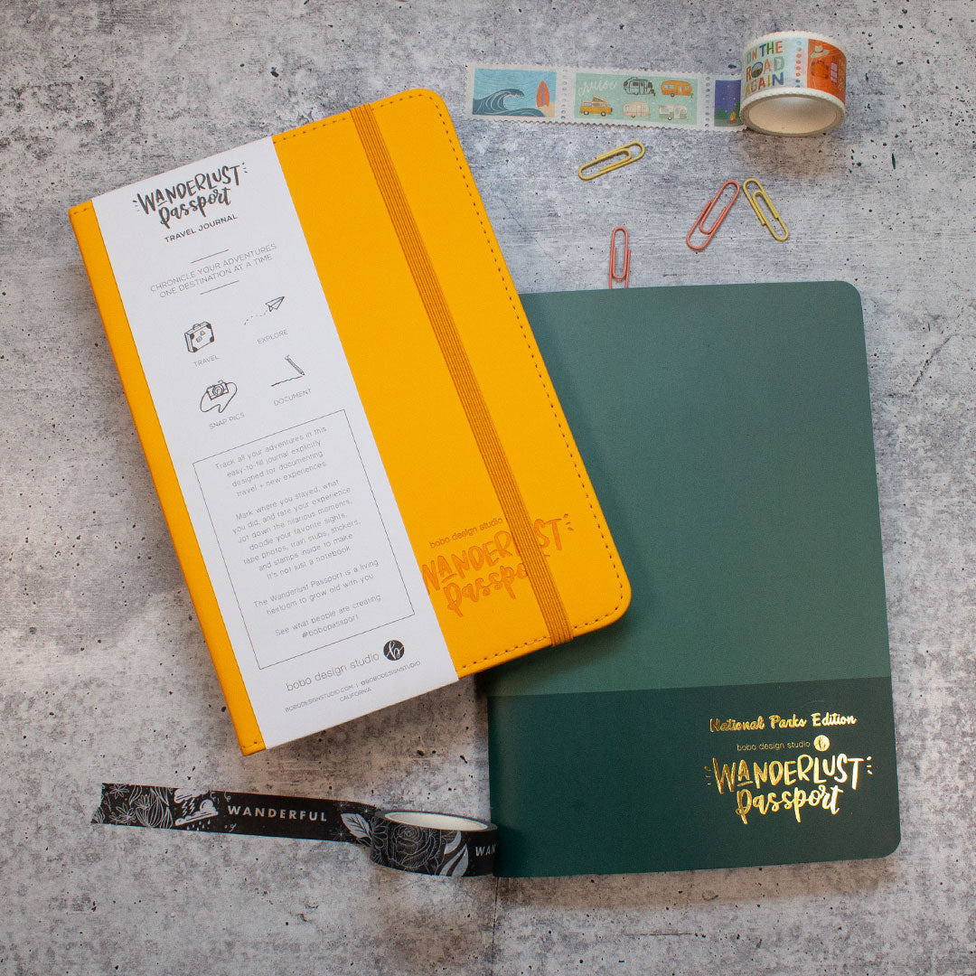 a wanderlust passport on top of a national parks wanderlust passport with a rolled out washi tape above with paper clips and a rolled out washi tape below