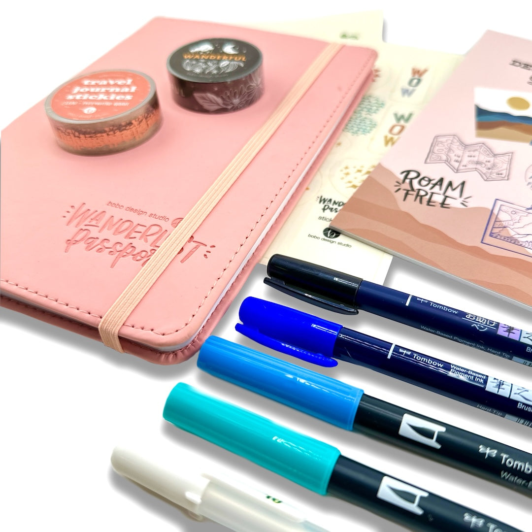 pink wanderlust passport with two washi tapes on top next to two sticker sheets and five pens