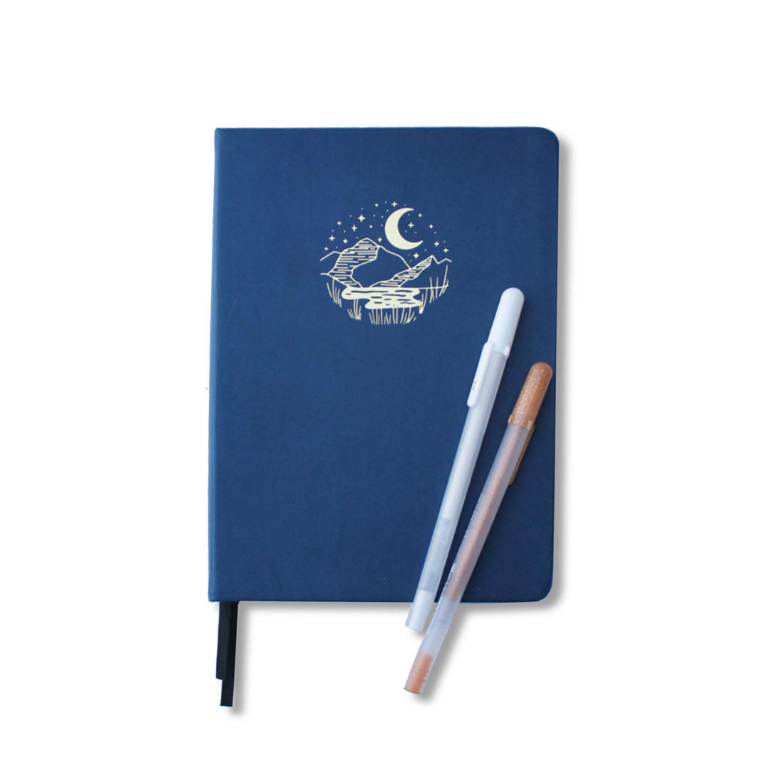 Black paged journal with leather blue cover with two gel pens laid on top