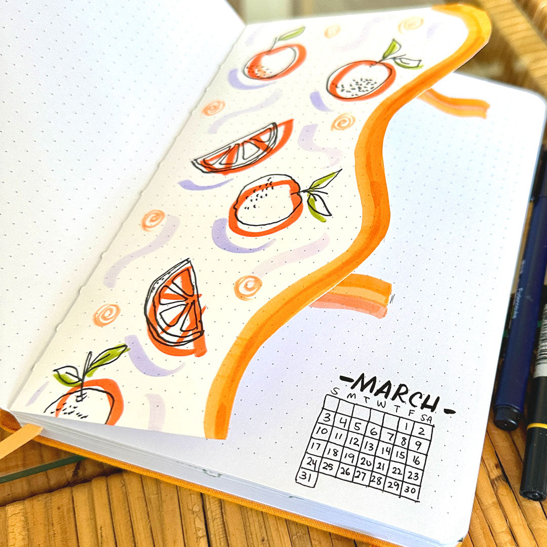 open dot grid journal with a page cut out with drawings of oranges and a small drawing of the month of March calendar