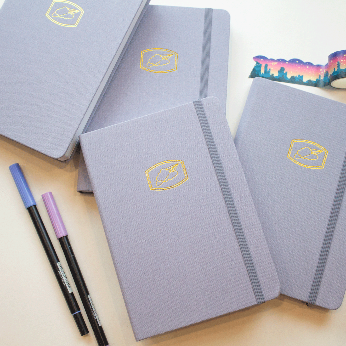 four cloud nine journals stacked on one another with two pens and a rolled out cloud cut southwest sunset washi tape