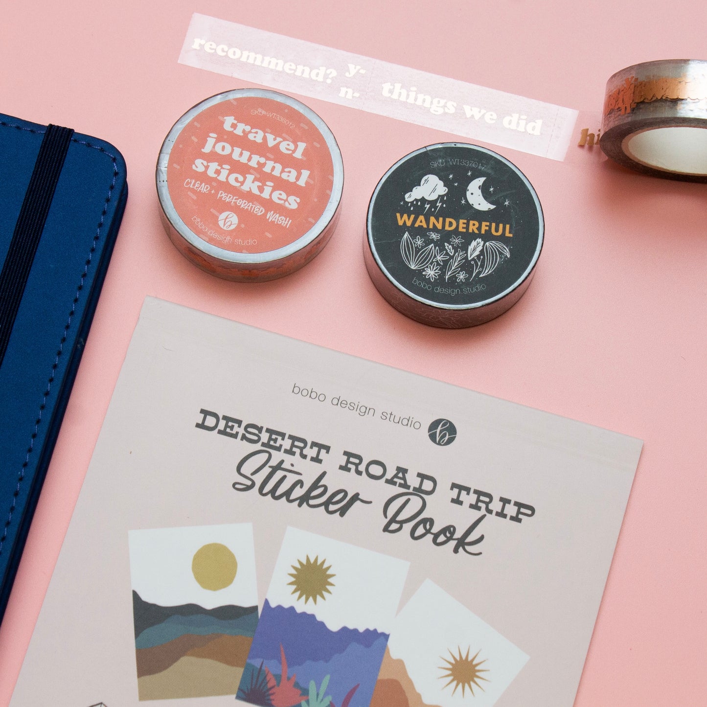 desert road trip sticker book next to a blue wanderlust passport with a black wanderful washi tape and a clear travel journal stickies washi tape and an open clear travel journal stickies washi tape on top