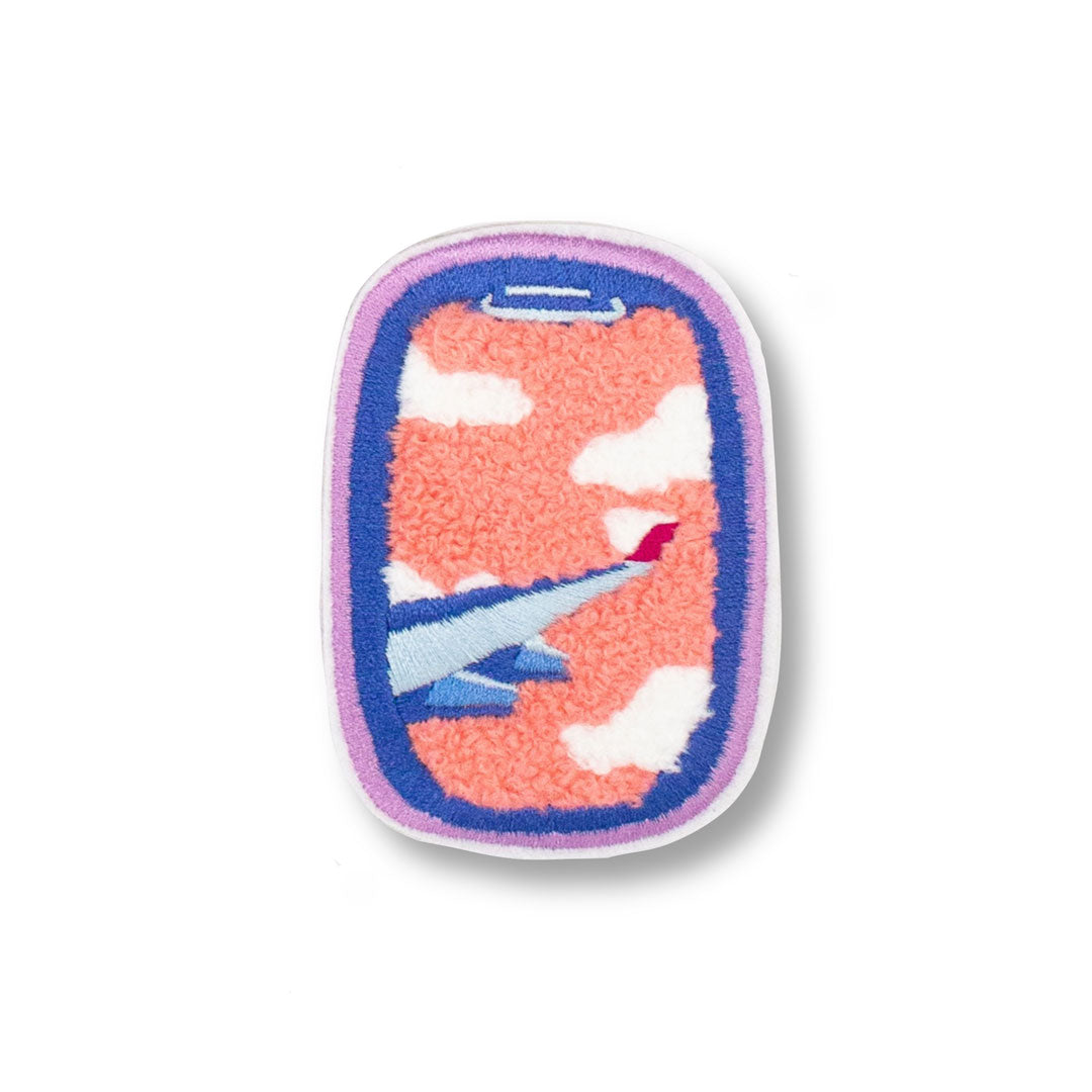 photo of a woven chenille patch in bright pinks and purples
 that feature an airplane wing through the view of an airplane window flying