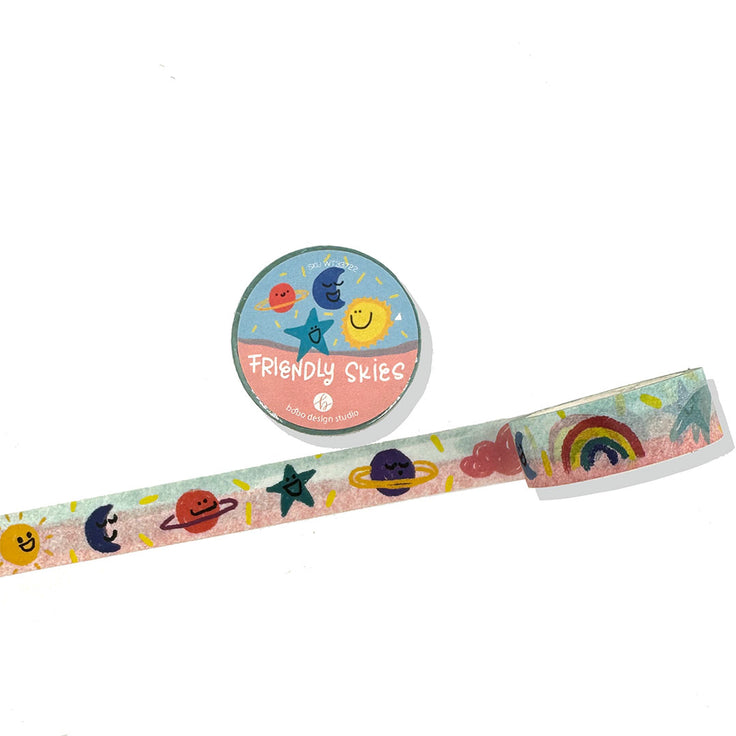 friendly skies washi tape rolled out it has a blue pink background with stars, suns, moons, planets, rainbows, and clouds. they each have a different expression