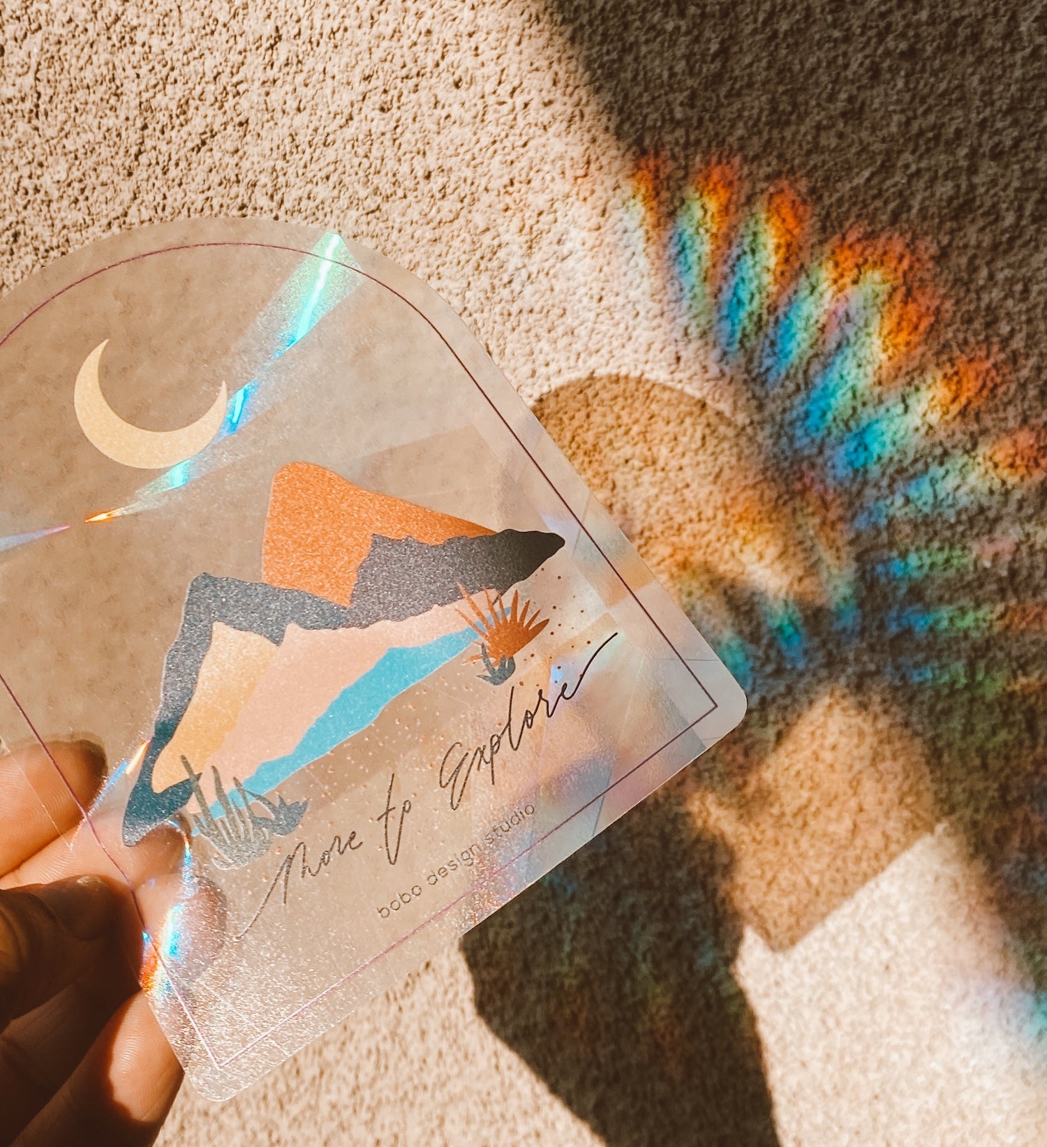 left hand holding more to explore sun catcher outside in the sun showing the rainbow reflection