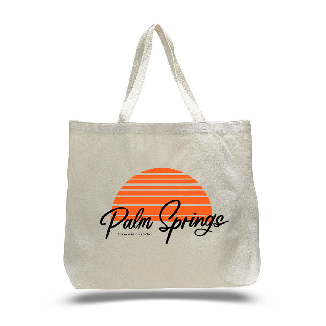 white cream colored canvas tote bag with "palm springs" written in black font cursive with an orange half circle that looks like a top part of a sunset