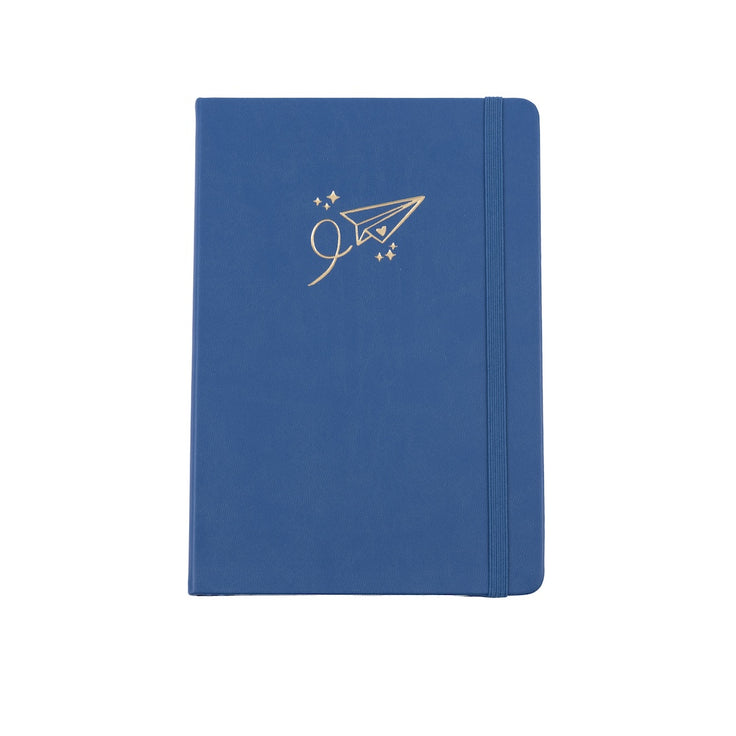 The A5 bobo Black dot grid journal in "airplane" with a medium blue vegan leather cover. A gold foil paper airplane with a heart and stars is stamped onto the front cover. A blue elastic closure is holding the journal shut.