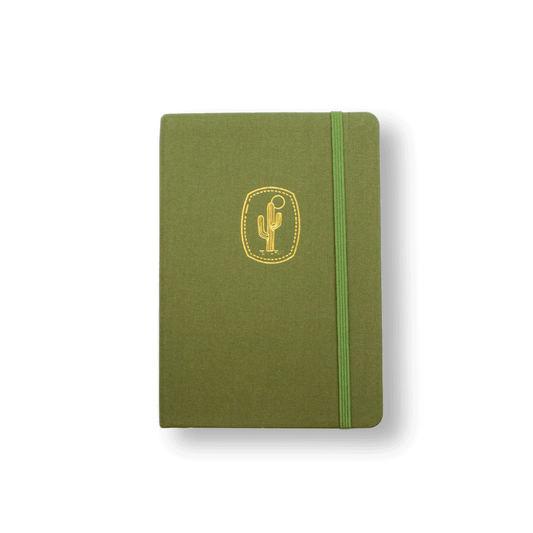 The A5 bobo dot grid Bujo journal in "Cactus" with an cactus green cover. A gold foil Saguaro Cactus and sun illustration is stamped onto the front cover. A corresponding green elastic closure is holding the book closed.