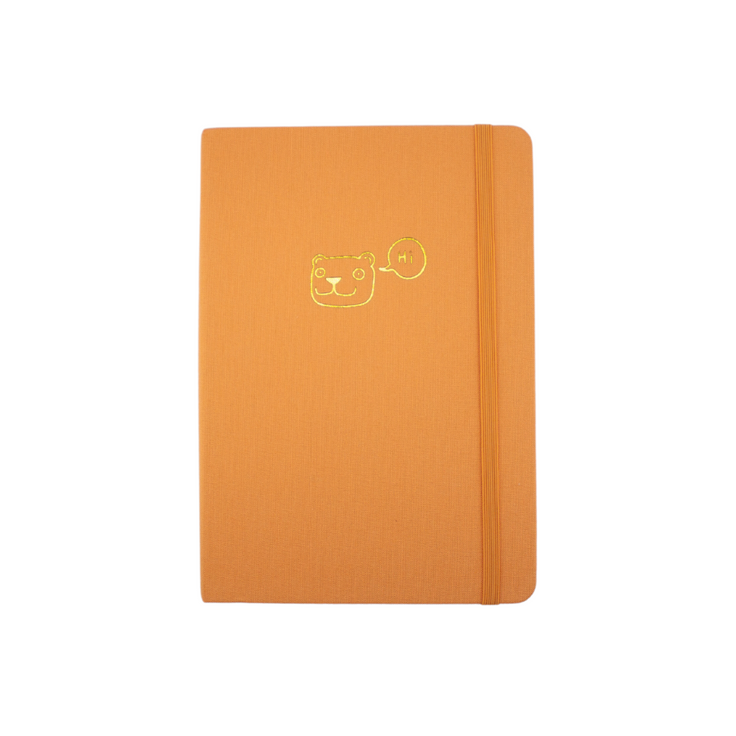 The A5 bobo Lined Journal "Tiger" with a tangerine orange linen cover. A gold foil smiling cartoon tiger head with a speech bubble with "Hi" inside, is stamped onto the center of the front cover. A corresponding orange elastic is holding the book closed.