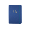 The A5 bobo Lined Journal "Whale" with a deep blue linen cover. A gold foil illustration of a humpback whale in the water under a starry night sky is stamped on the cover. A corresponding medium-dark blue elastic is holding the journal closed.