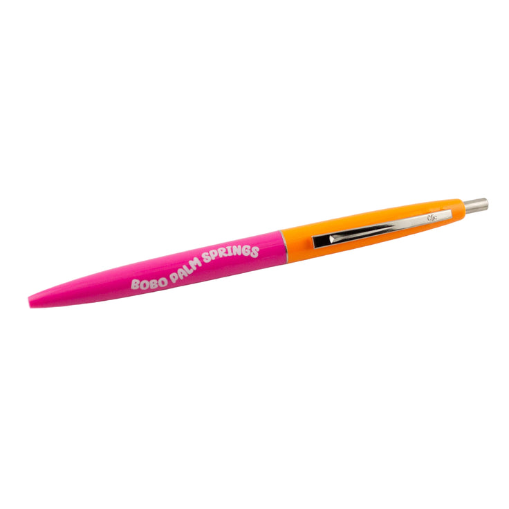 A bright pink and orange ballpoint pen with a silver click top, labeled 'bobo Palm Springs'.