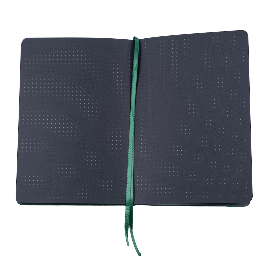 The bobo Black Dot Grid journal is open to a page spread to show the black pages inside. Faint white dots gridding each page can be seen. The pages have rounded outside corners to match the book cover. A green ribbon bookmark runs down the center between the two pages.