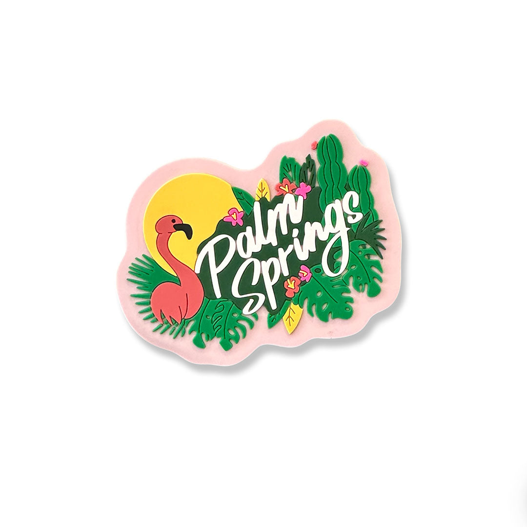 Palm Springs flamingo magnet. features a flamingo with a sun behind it and leaves with some cactus and "palm springs" written in white cursive letters with a pink background