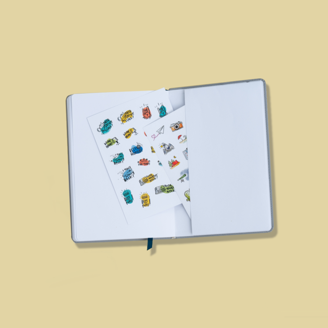 The Wanderlust Passport is opened to the last page and back cover. There is a paper pocket attached inside the back cover that has the two included sticker sheets inside. The stickers include small drawings of a mountain, a camera, a paper airplane, a tent in the forest, and other travel images and sayings. The ribbon bookmark is visible protruding from the bottom of the journal.