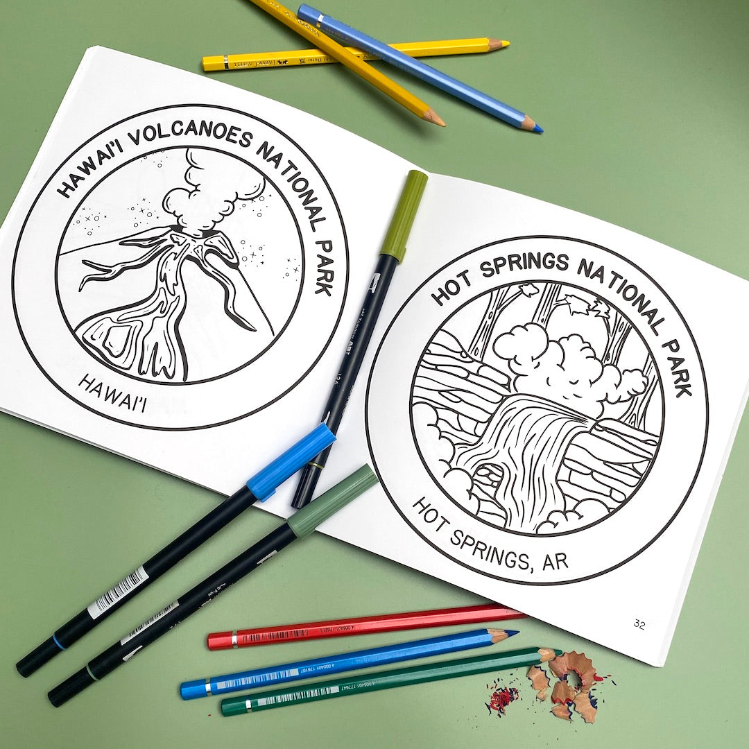 The National Parks Coloring book is open pages 31 and 32. The left page has a black line-work drawing of Hawai'i Volcanoes National Park and the right page has a drawing of Hot Springs National Park, AR printed on the white pages. Coloring pencils and markers are nearby.