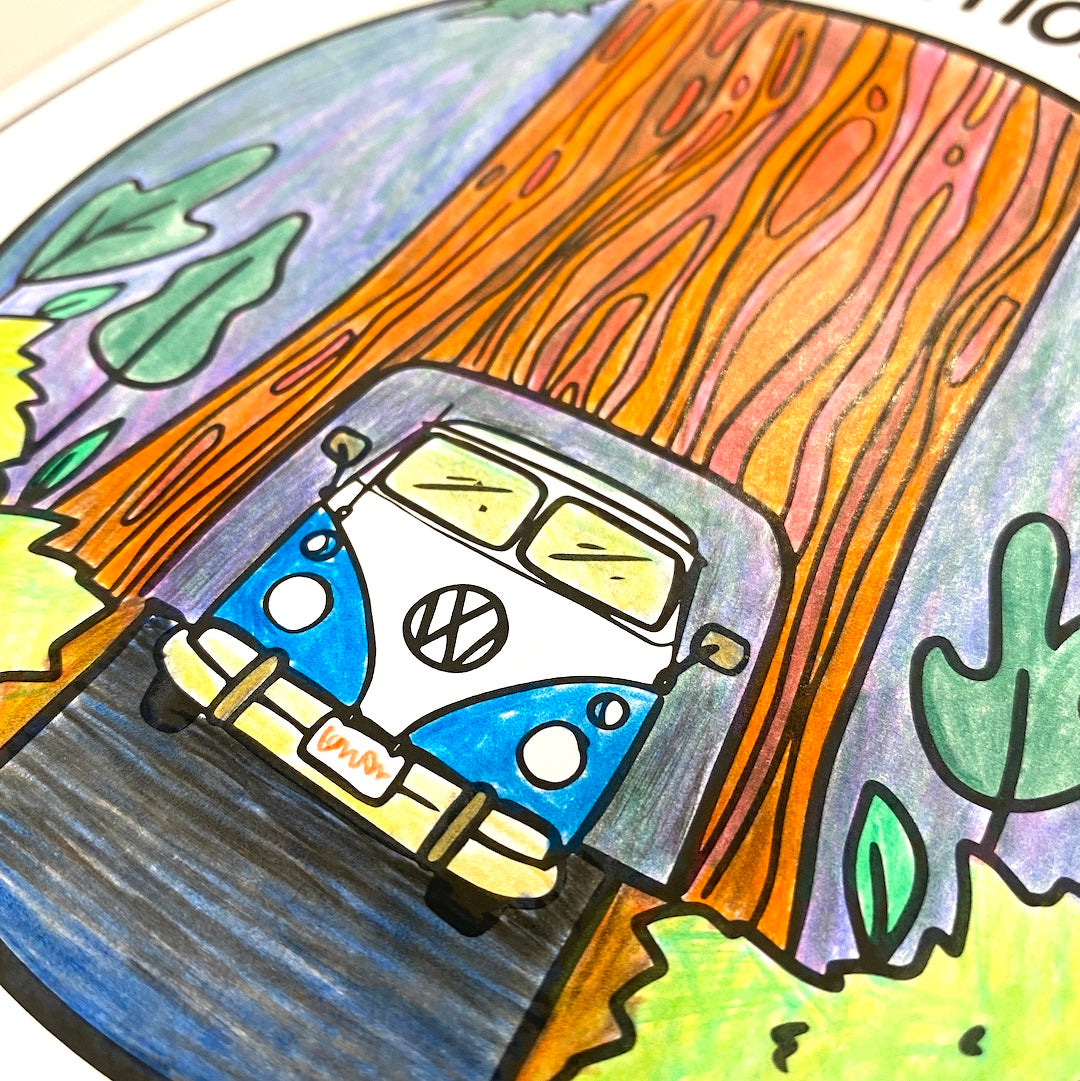 A page from the National Parks Coloring Book has been colored in with coloring pencils and depicts a blue retro bus driving through a redwood tree tunnel.