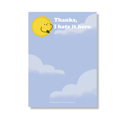 5 inch by 7 inch notepad. The background is light blue with three pale blue-white clouds. A yellow sun with a flat expression and cartoon arms with hands intertwined is looking at the text "Thanks, I hate it here." in white at the top of the page. A small logo that reads "@bobodesignstudio @bobopalmsprings" is at the bottom of the page. 