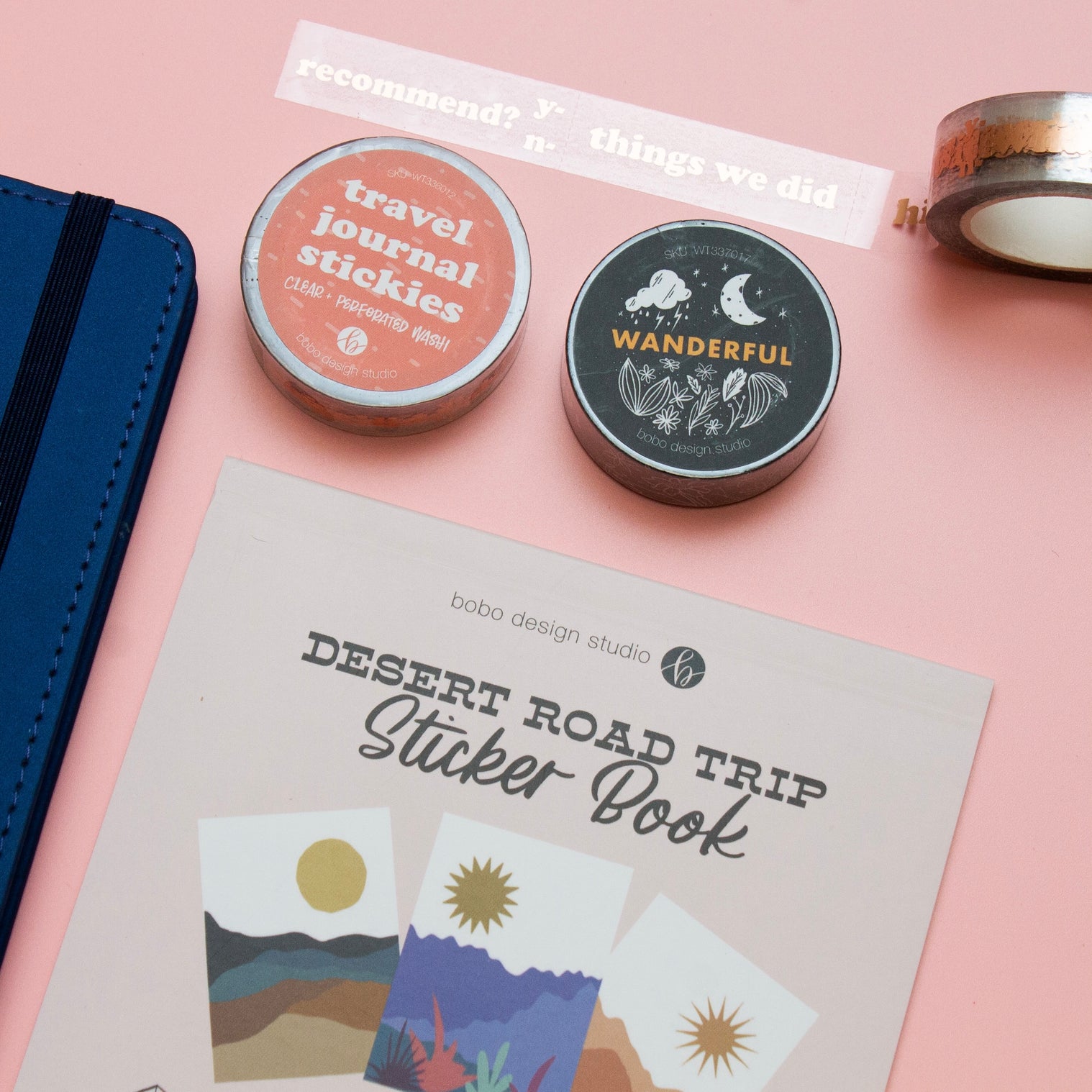 desert road trip sticker book next to a blue wanderlust passport with a black wanderful washi tape and a clear travel journal stickies washi tape and an open clear travel journal stickies washi tape on top 