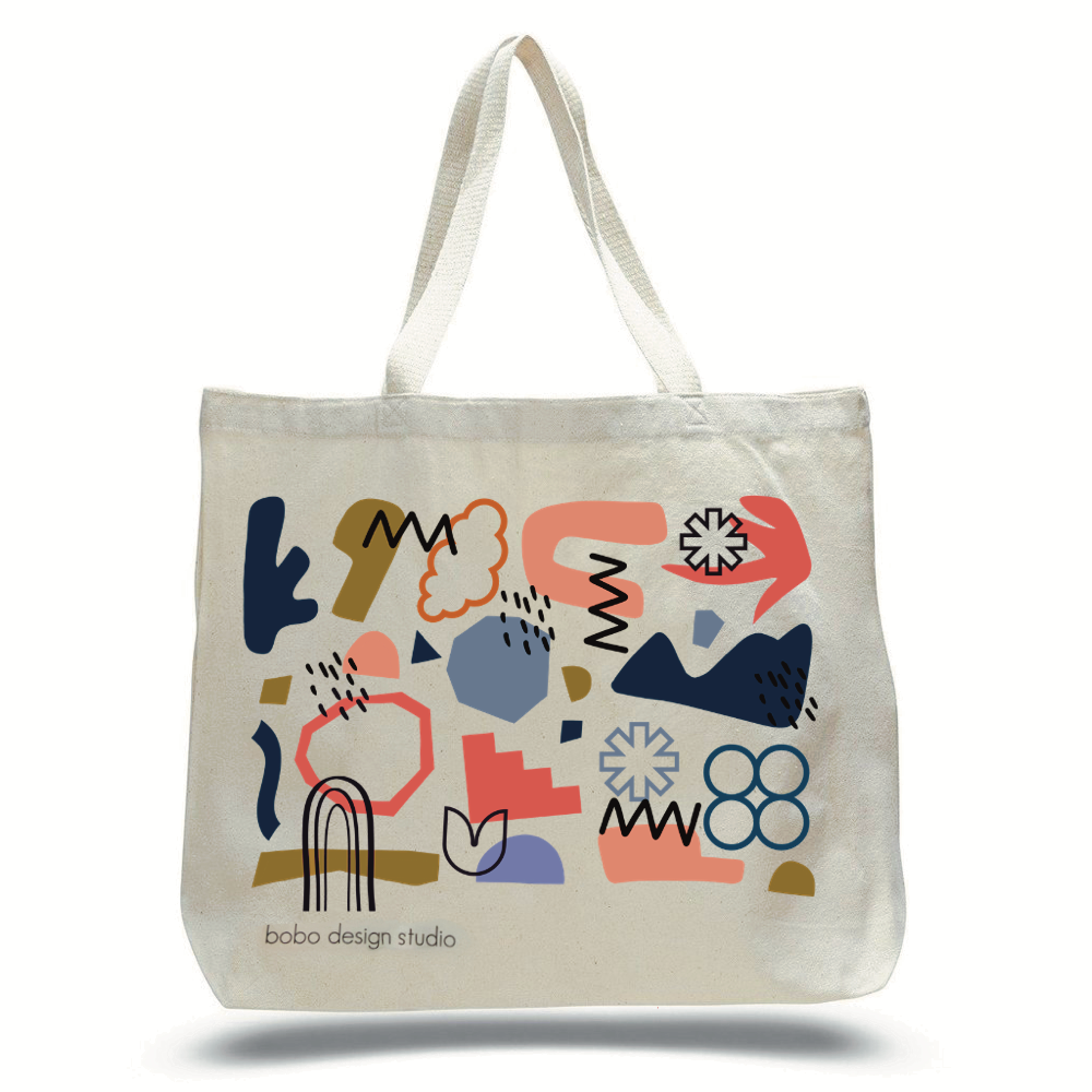 Large natural canvas colored tote bag with a composition of abstract shapes printed on the side. Navy blue, grey-blue, grey-brown, orange, coral pink, and  black overlapping shapes are printed on the side with the words "Bobo Design Studio" printed in small text below. 