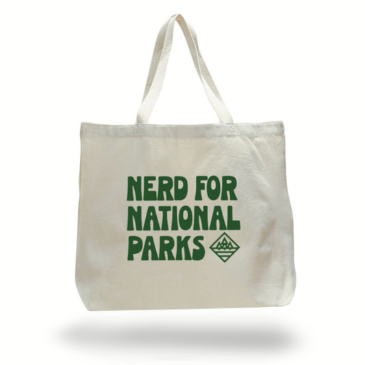 Large natural canvas colored tote bag with "NERD FOR NATIONAL PARKS" printed in green on the side. A small simple image of 3 trees in a diamond shape is printed beside the word PARKS.